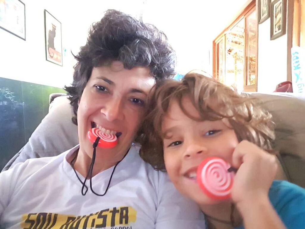 Eu e Leon estamos olhando para a camera, sorrindo, cada um com um mordedor na boca em formato redondo como se fosse um doce.